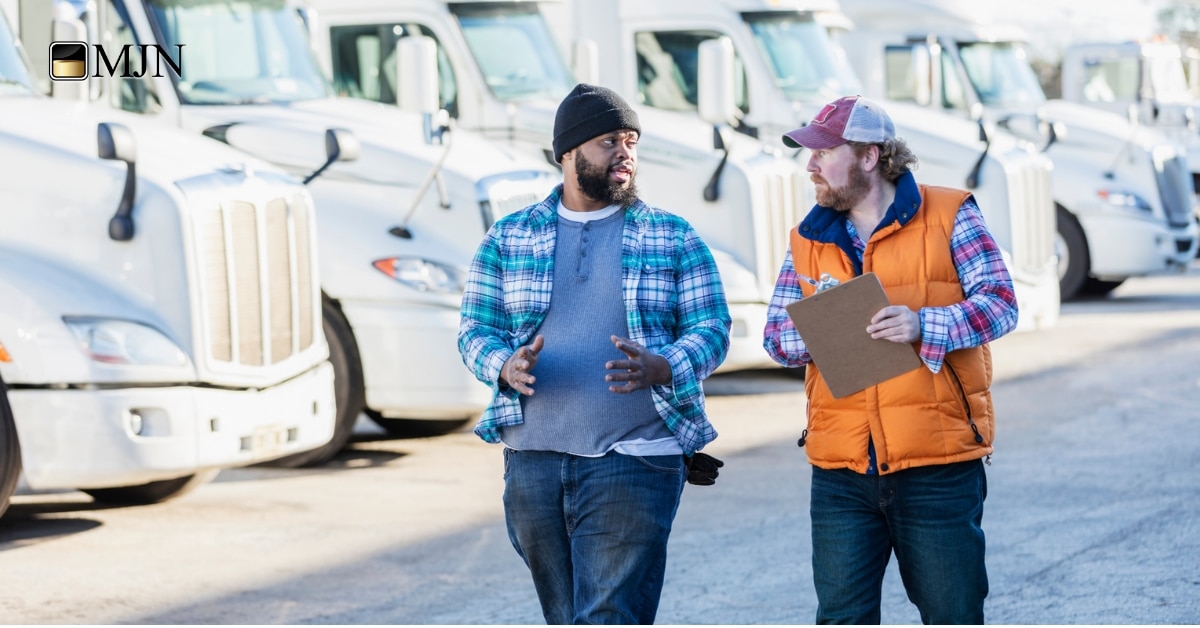 Truck driver reviewing freight invoices beside a semi-truck